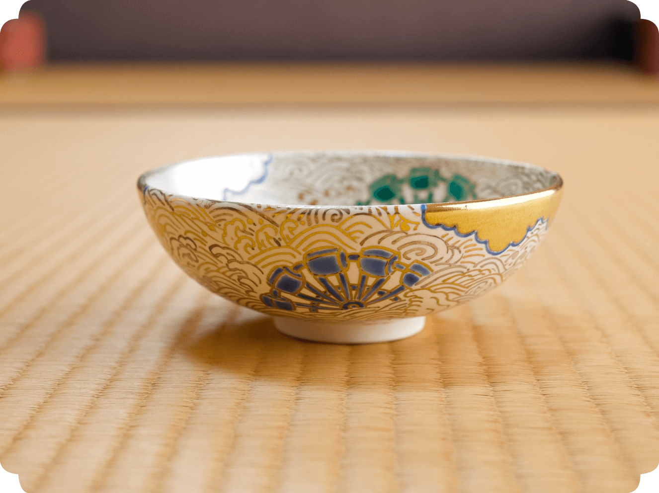 金と緑で華やかに装飾された茶碗が畳の上に置かれている